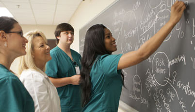 nursing professor working with students at a blackboard